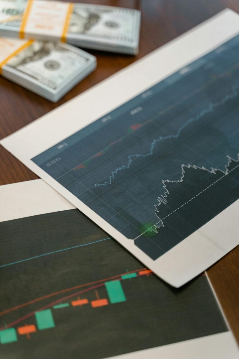 Papers with financial graphs beside stacks of US dollar bills representing market analytics.